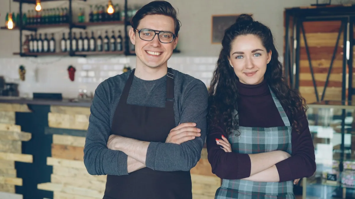 Dos propietarios de una cafetería de barrio sonriendo dentro de su local