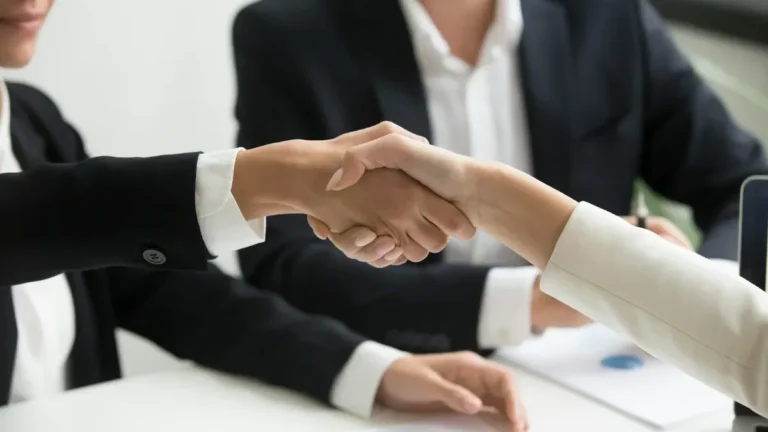Dos profesionales se dan la mano frente a un portátil tras cerrar un acuerdo