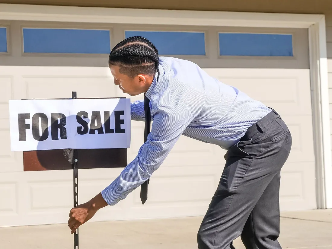 Agente colocando un cartel de venta en una vivienda